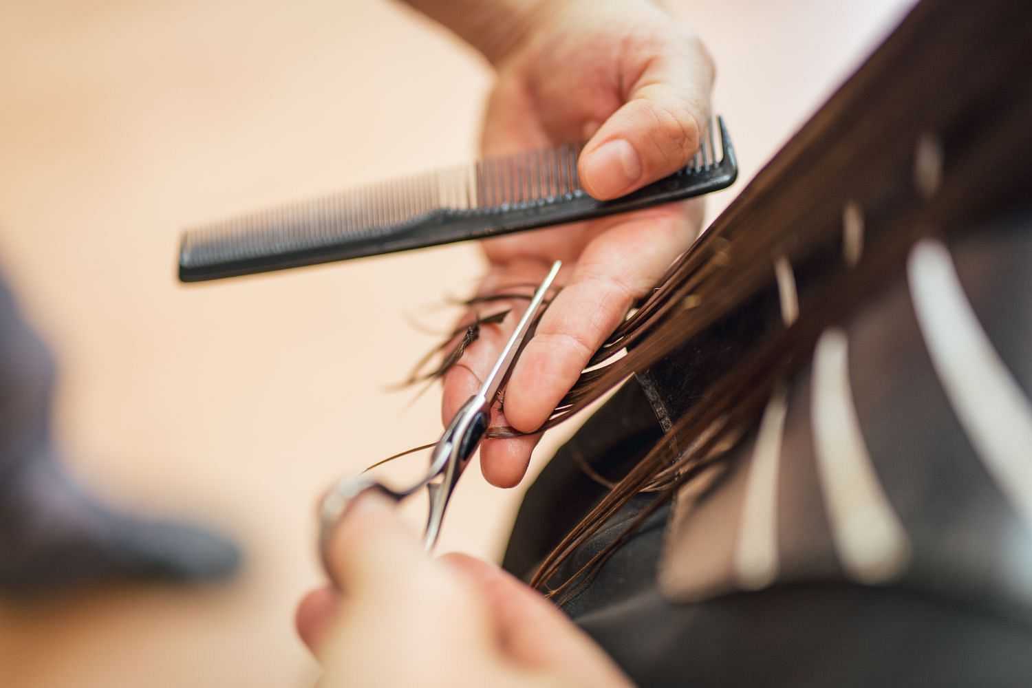 Close-up of a hairstylist's hands cutting a client's hair with scissors and a comb.