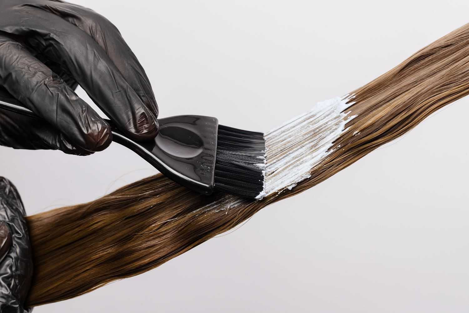 Applying hair dye with brush to brown hair strands, close-up view.