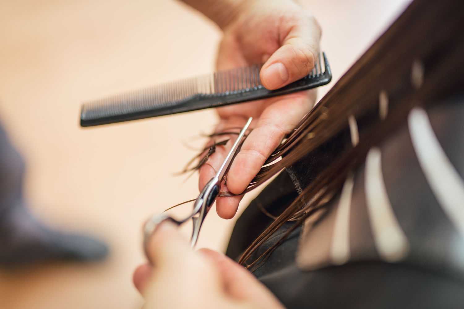 Close-up of a hairstylist's hands cutting a client's hair with scissors and a comb.
