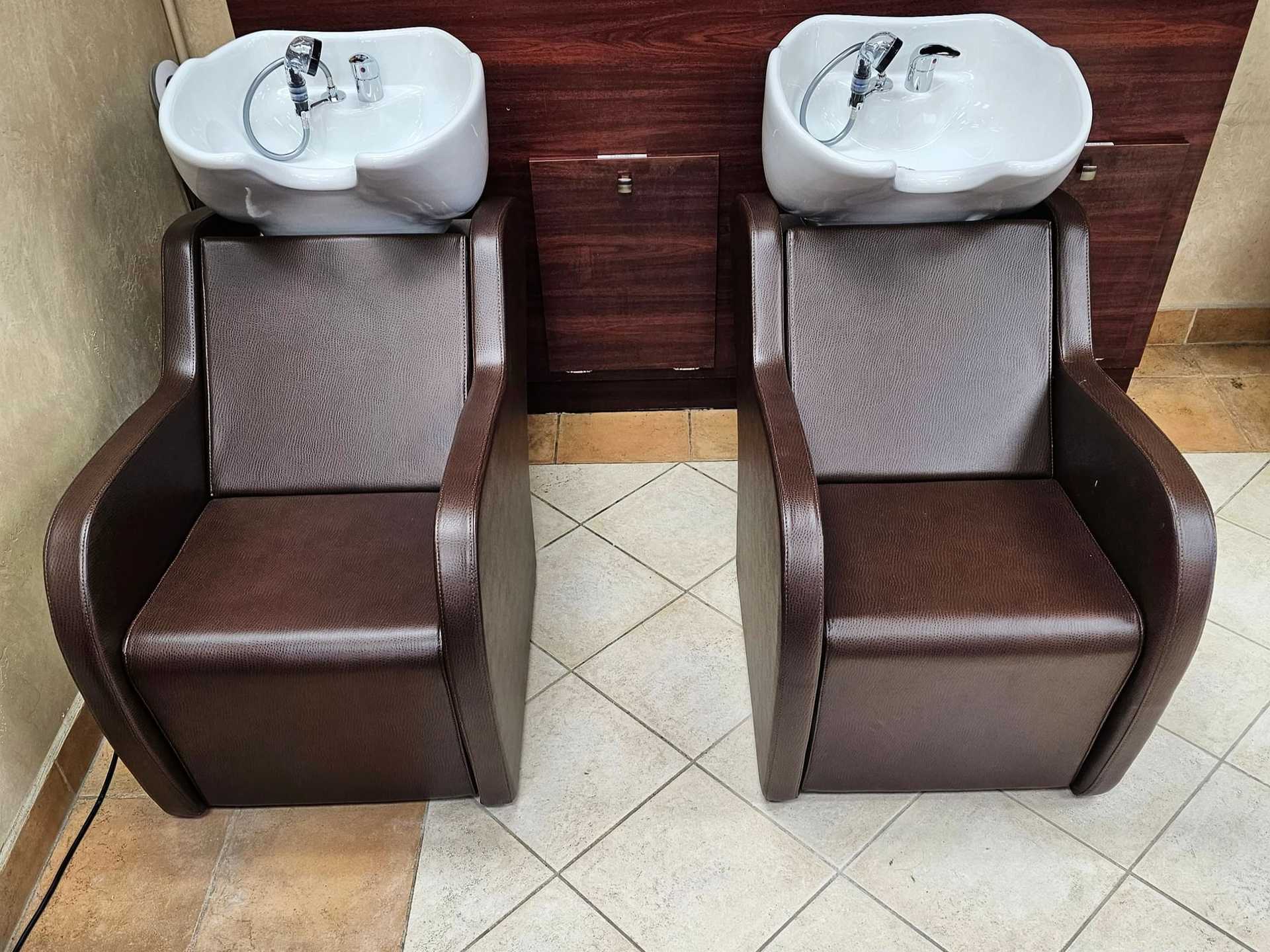 Two brown salon hair washing chairs with white sink basins against a wooden backdrop.