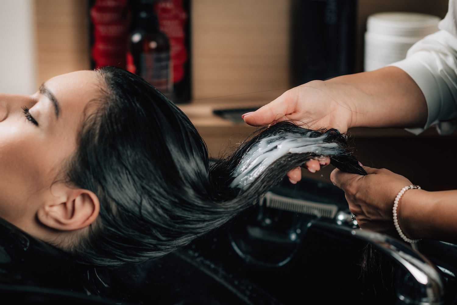 A woman getting her hair washed at a salon with shampoo being applied by a hairstylist.